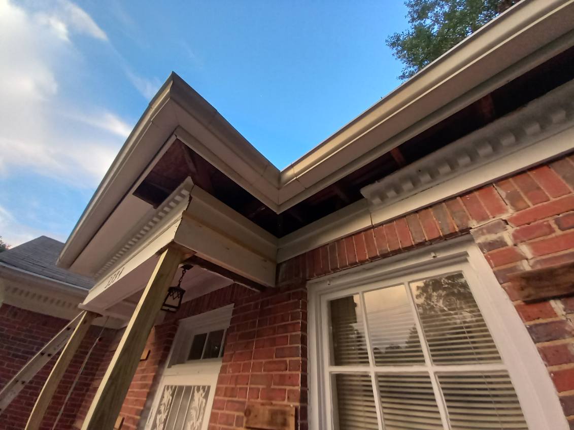 Exterior corner of a brick building with new white fascia boards and dentil molding fitted, the wooden roof sheathing still exposed