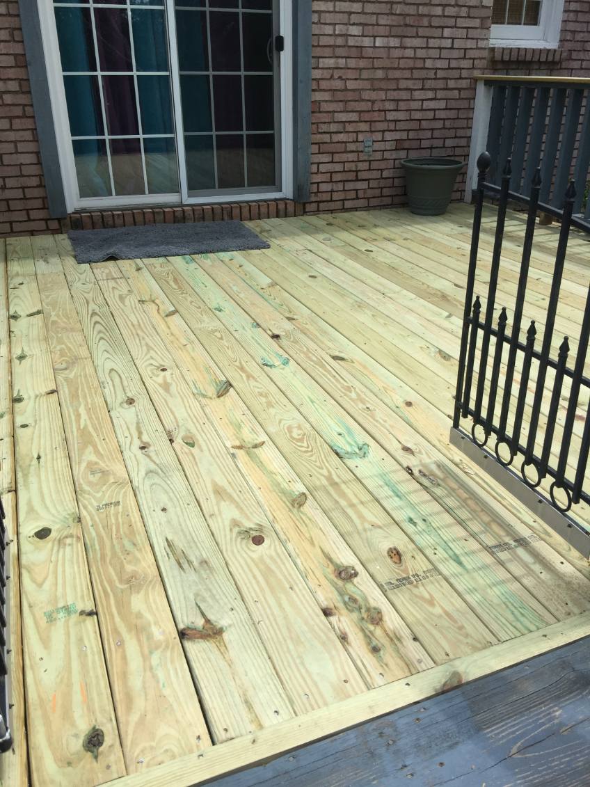 New deck of diagonally laid pressure-treated pine boards against a red brick wall with a sliding glass door