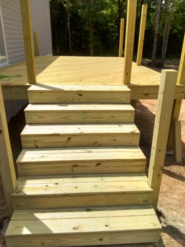 Newly constructed light wooden stairs with six steps leading up to a deck against a house
