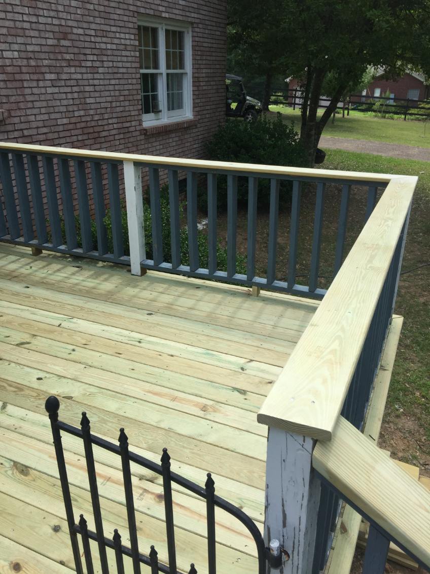Wooden deck with light unfinished planks and a two-tone railing of gray-blue balusters under a light wood top rail, with a black metal gate