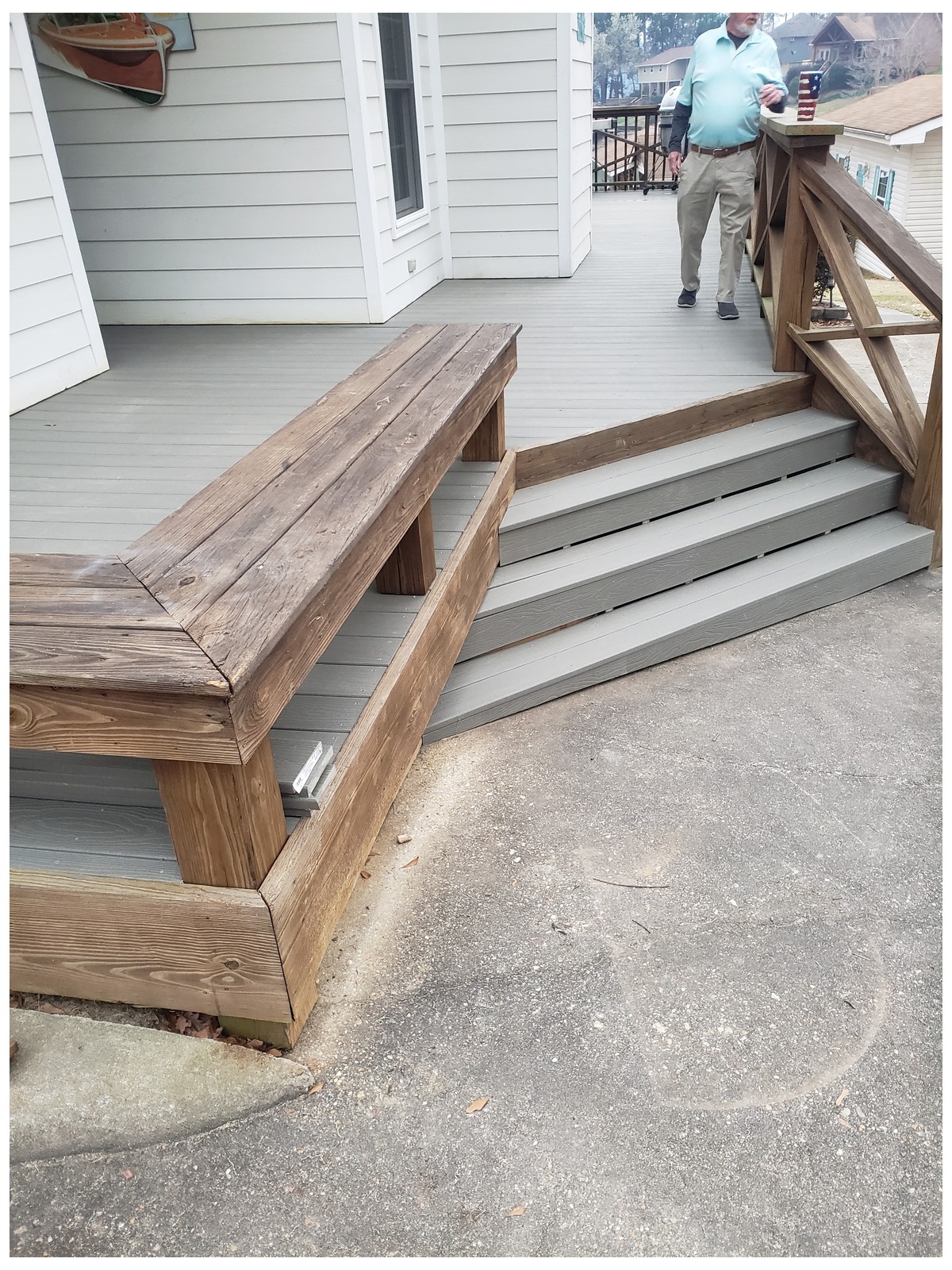 Grey-finished wooden deck with a built-in wooden bench and steps leading down to a concrete driveway