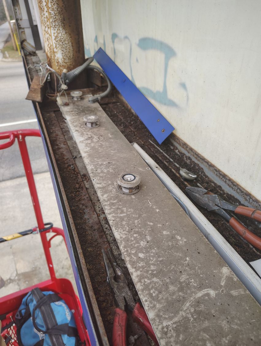 Sliding gate track opened up with the rollers and bearings exposed, tools and a plate laid out beside it