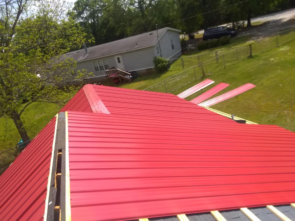 Bright red metal roof panels mid installation with white and yellow underlayment strips still exposed at the bottom edge