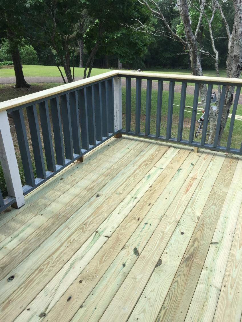 New wooden deck with light pressure-treated boards and a railing with dark gray balusters, white posts and a light wood handrail