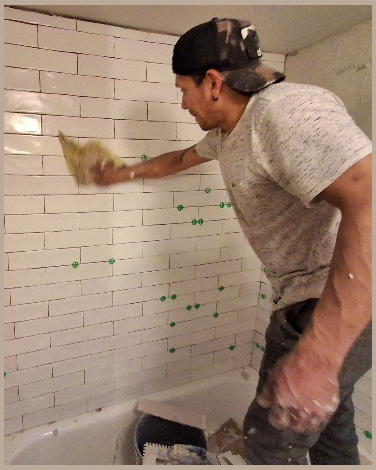Chris wiping newly set white wall tile clean in a bathroom during a remodel in Montgomery