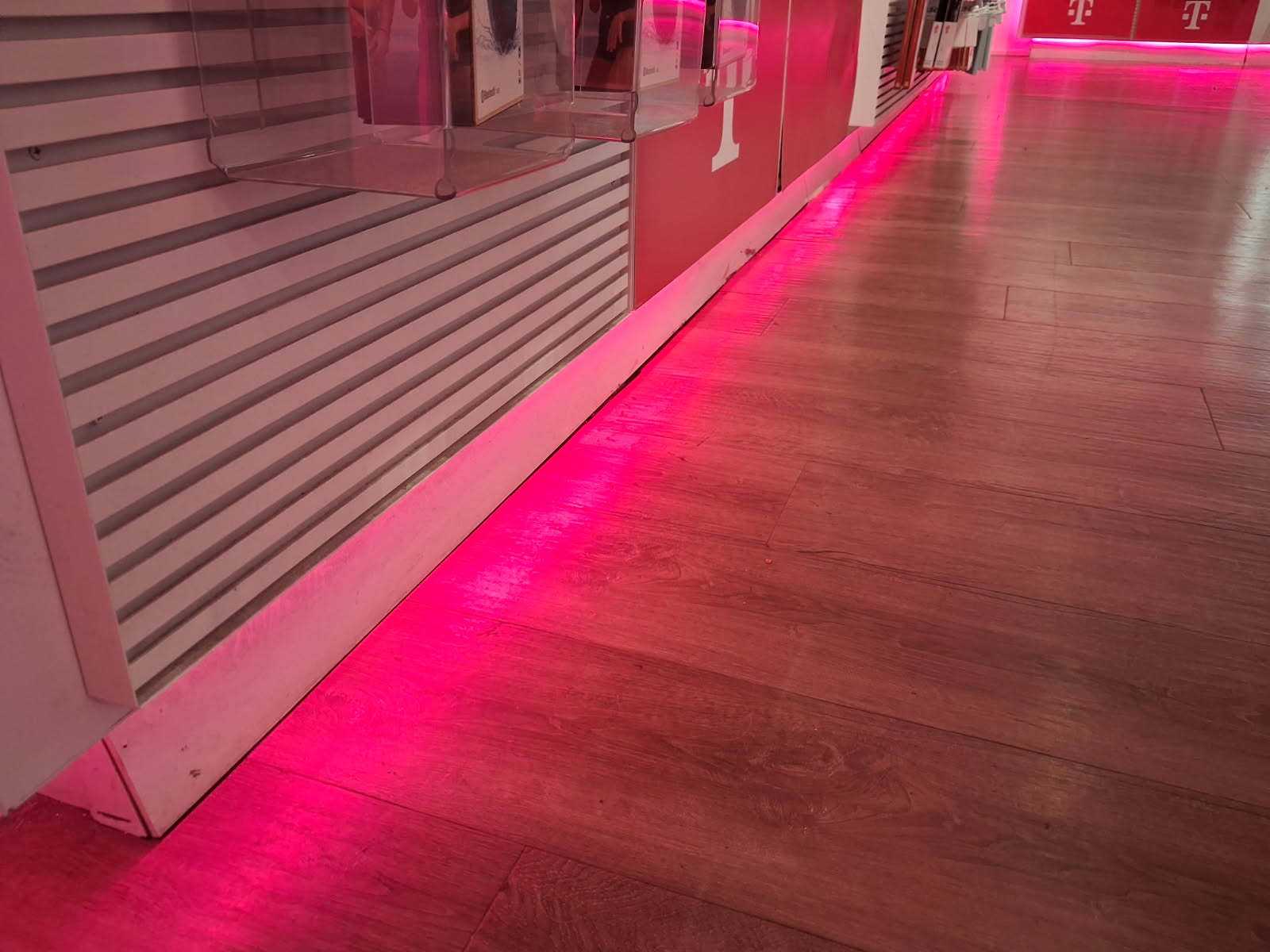 Retail store wall finished with slatted display panels and clear acrylic holders above a solid base panel, with accent lighting washing the plank floor