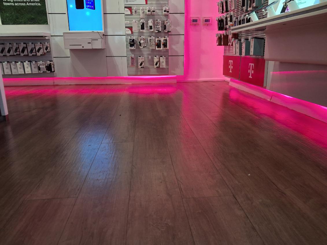 Retail store interior with wood-grain flooring, white wall display panels and a lit strip running along the base of the counters
