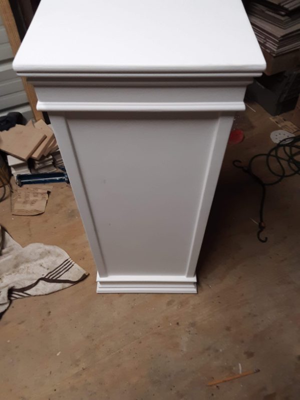 Tall white painted pedestal cabinet standing on a concrete workshop floor