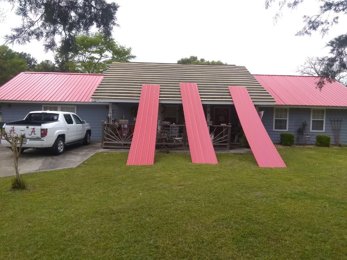 Single-story house with a two-tone metal roof and three large pink roof panels standing on the lawn ready to be fitted