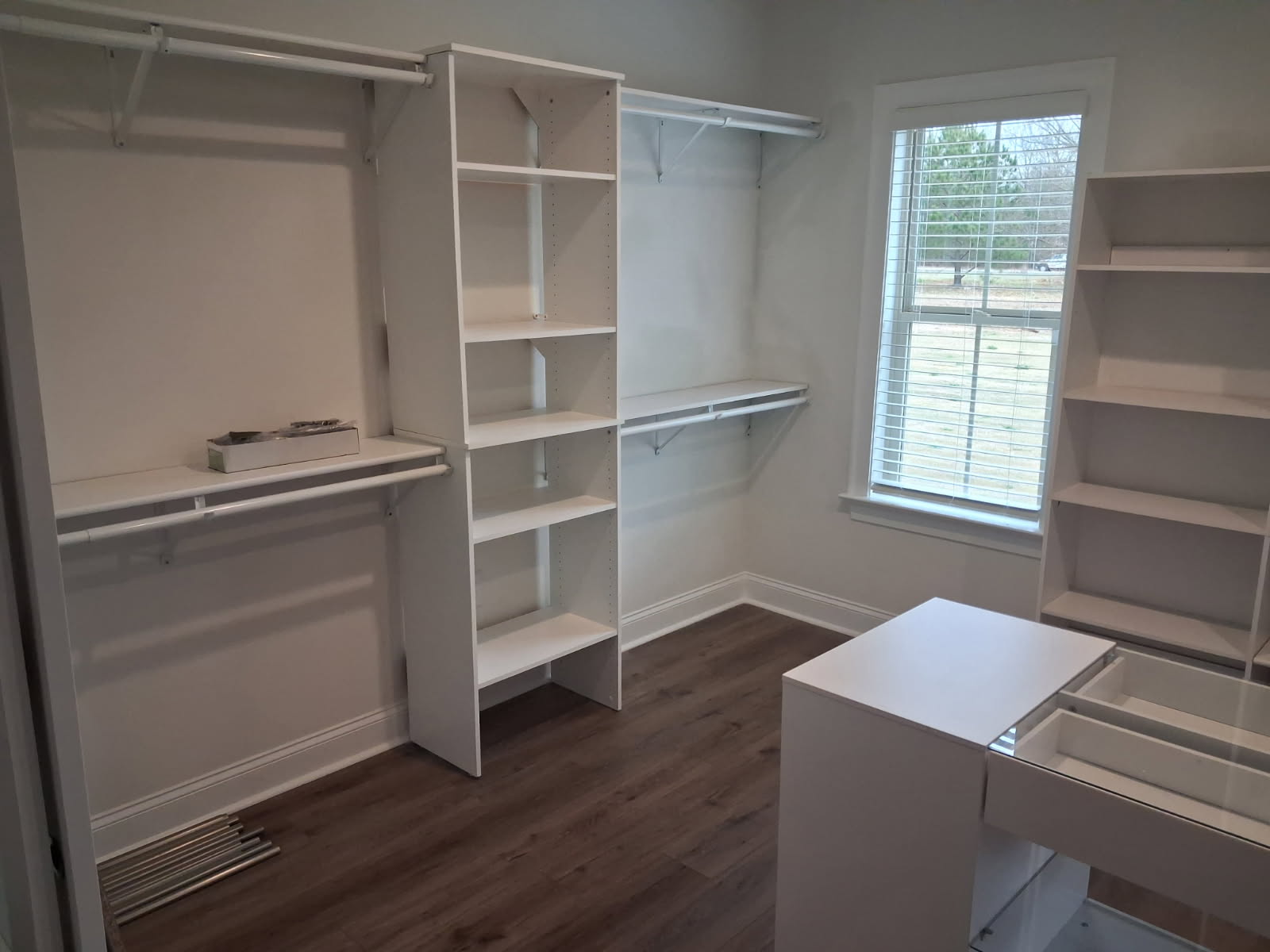 Finished walk-in closet with shelving towers, hanging rods and a center island, on dark plank flooring