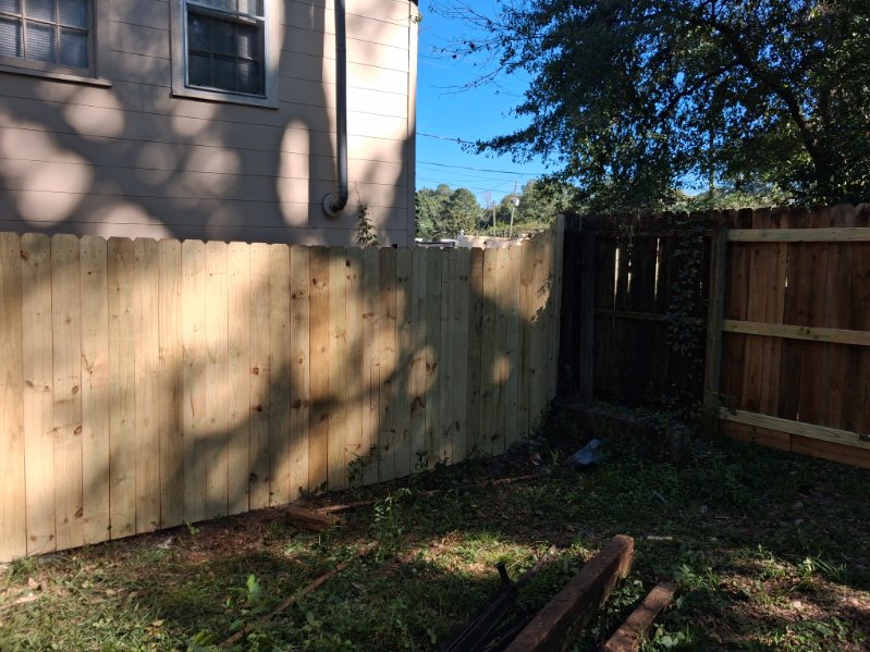Newly built light wooden privacy fence with a scalloped top edge meeting an older darker fence in a backyard
