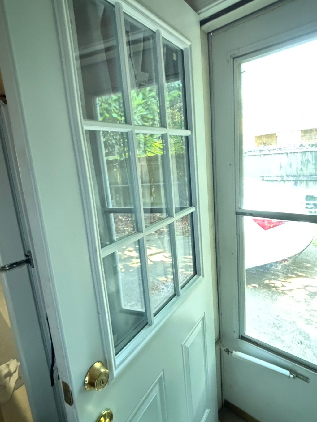White interior nine-pane door standing ajar beside a white storm door, opening onto a patio
