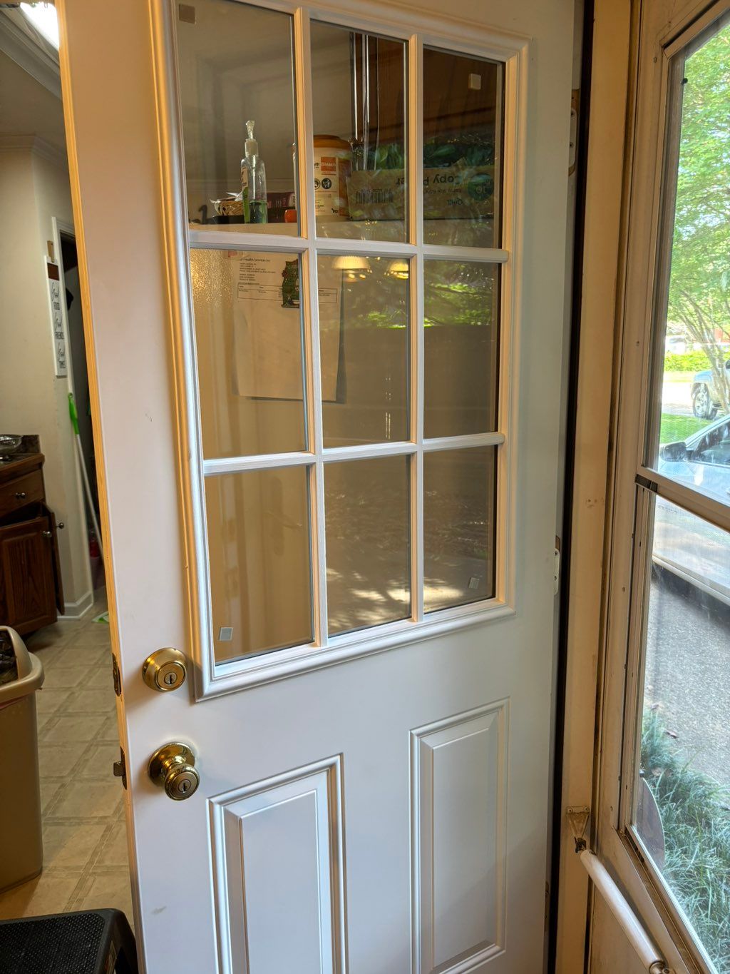 White nine-pane door hung square in a wooden frame with brass hardware, opening into a kitchen