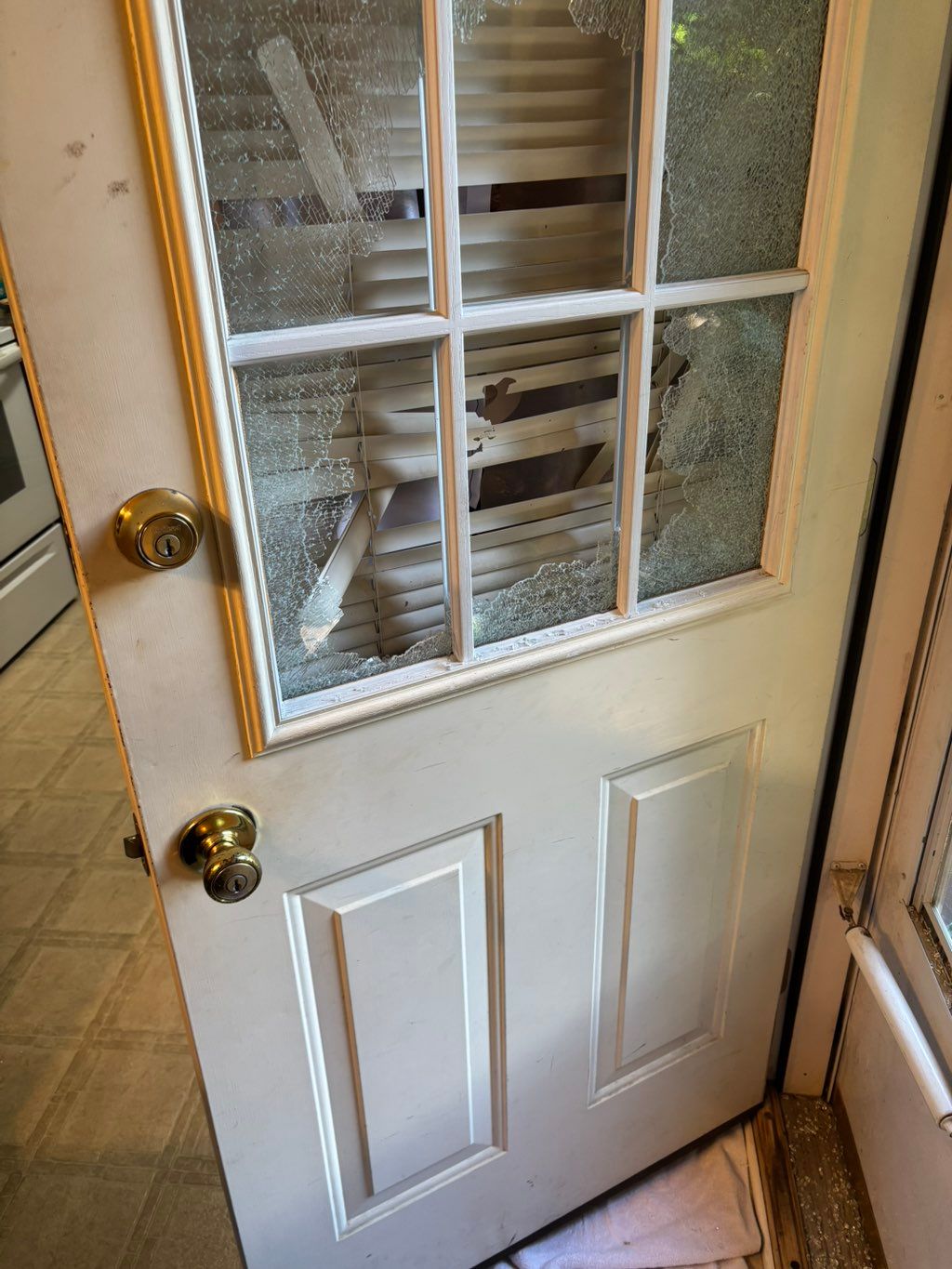 White exterior door with a broken lower glass pane and brass lockset hardware